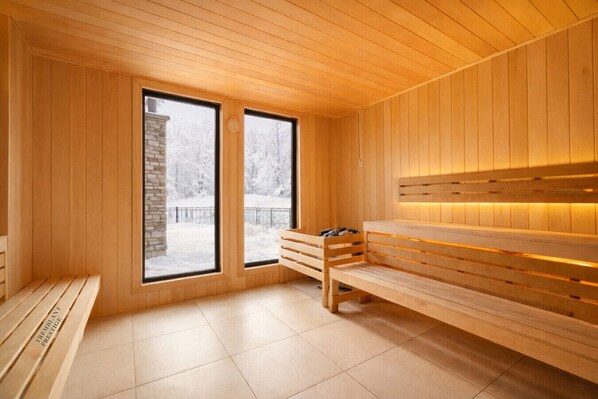 A sauna room with wooden benches, large windows, and a tiled floor.
