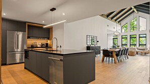 Eine moderne Küche mit einer zentralen Kochinsel, Edelstahlgeräten und einem Essbereich mit hohen Decken und großen Fenstern.