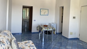 Un salon avec un canapé, une table à manger entourée de chaises, un petit coin cuisine et une salle de bain visible à travers une porte ouverte.