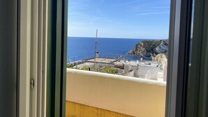 Une vue depuis une fenêtre donnant sur une zone côtière, avec un ciel dégagé et une vue lointaine sur la mer.