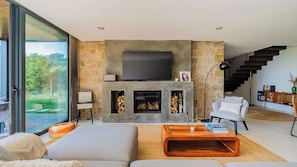 Una sala de estar moderna con chimenea, un televisor de pantalla plana grande y una escalera que sube a un nivel superior.