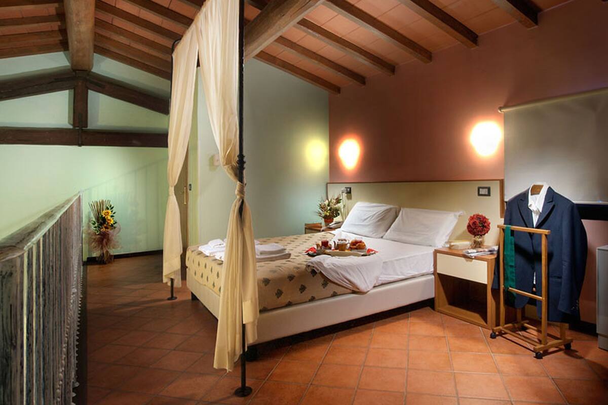 Une chambre à coucher avec un lit à baldaquin, une table de chevet avec une lampe, un miroir et un porte-manteau avec une veste.