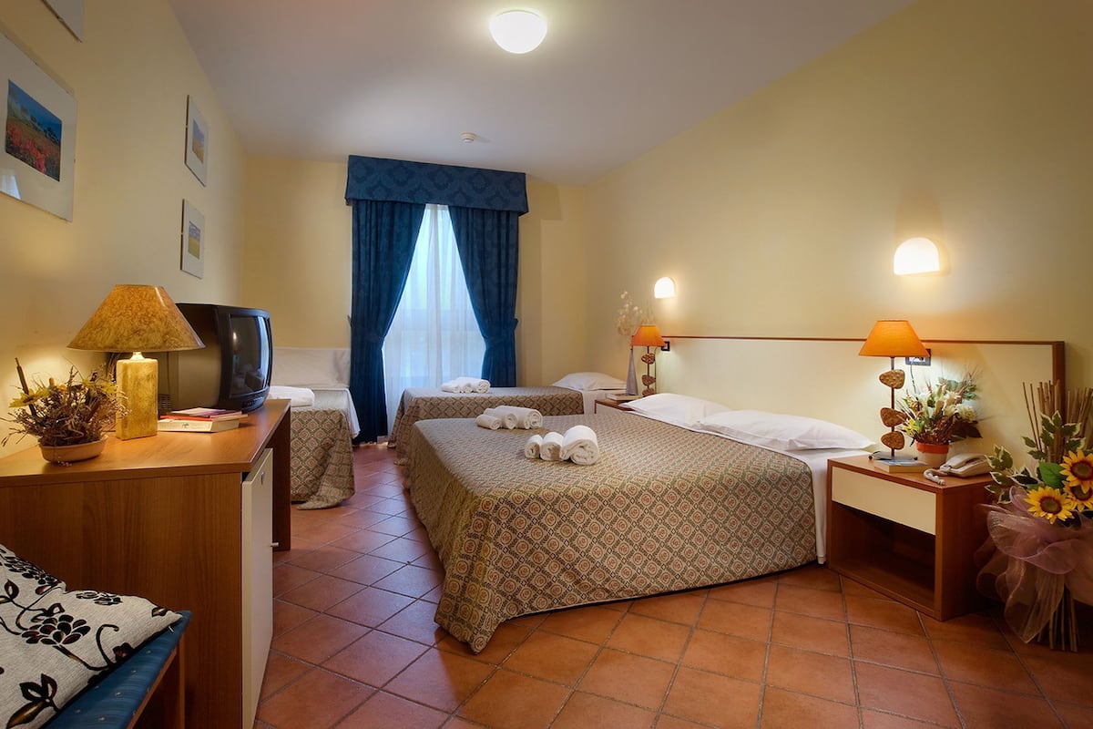 Une chambre d’hôtel avec deux lits, un bureau avec une lampe, une télévision et une petite table sur laquelle est posé un vase de fleurs.