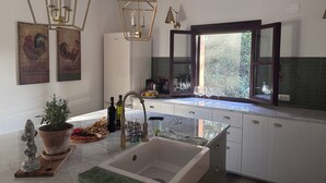 A modern kitchen with a large island, pendant lights, and a window with a view of greenery.