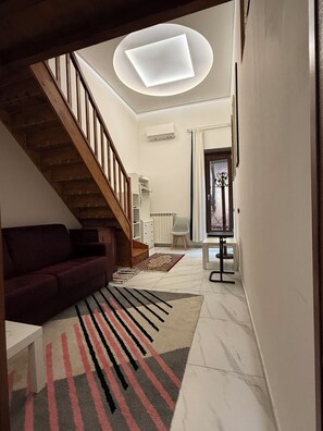 A modern living room with a staircase, a sofa, a patterned rug, and a ceiling light fixture.