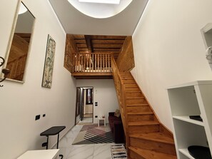 A modern interior with a wooden staircase, a small seating area, and a ceiling light.