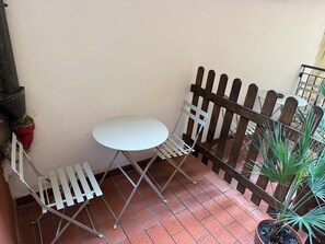 A small outdoor seating area with a white table and metal chairs, a wooden fence, and potted plants.