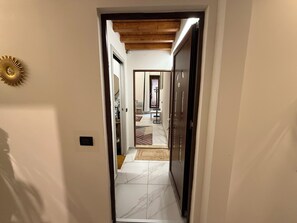 A hallway with a wooden ceiling, a marble floor, and a door leading to a room with a bed and a nightstand.