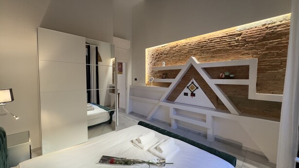 Et moderne hotelværelse med en murstensvæg, et sminkebord med spejl og en pænt redt seng med håndklæder.