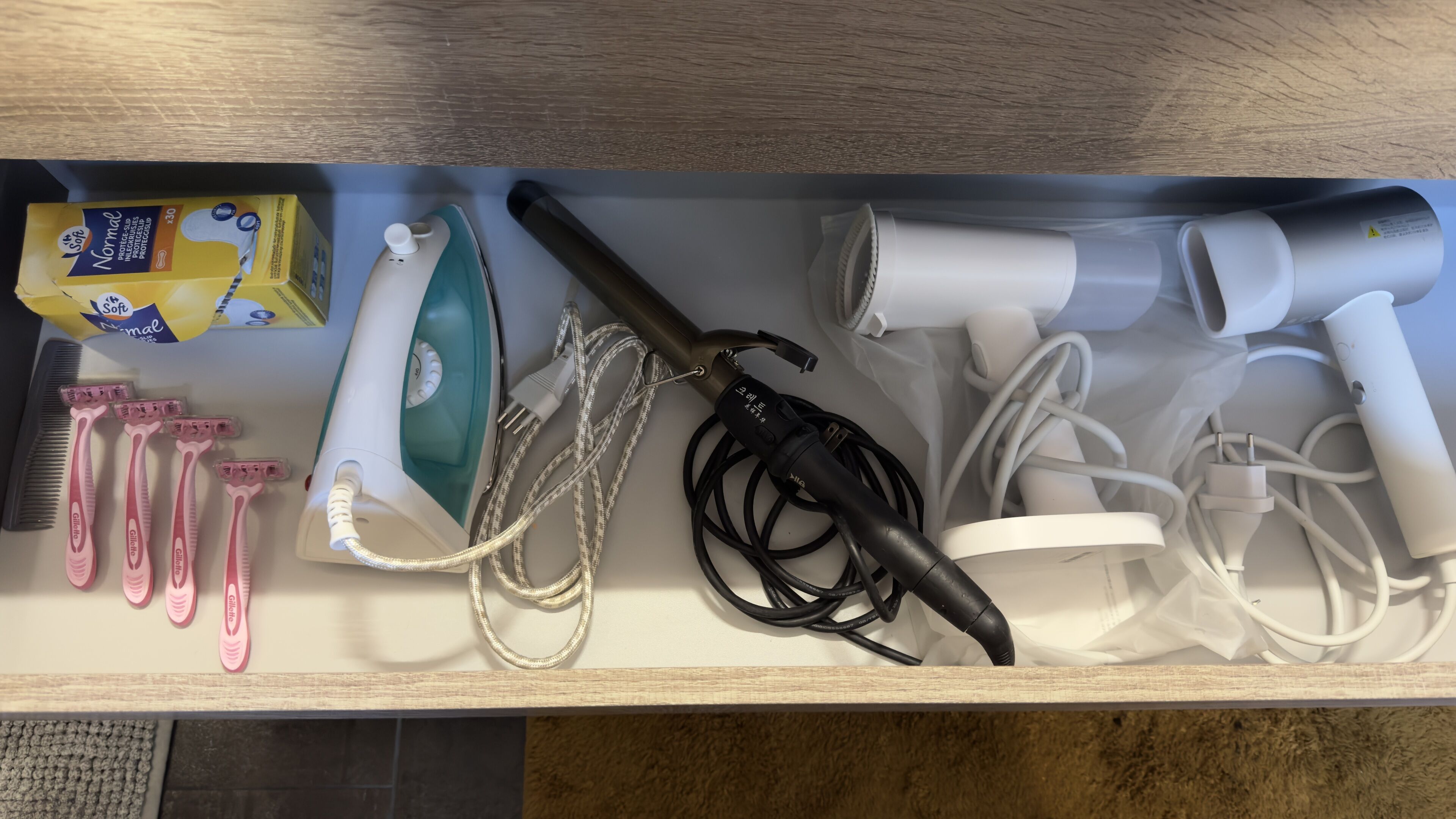 A drawer containing various personal care items including razors, a hairdryer, and a box of shaving cream.