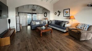 A spacious living room with a high ceiling, wooden flooring, a large sofa set, a coffee table, and a television on a wooden stand. - Luxurious Villa " Sea La Vie" in Pelican Key (Koolbaai)