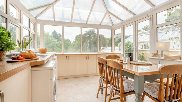 A conservatory with a kitchen area, including a dining table, chairs, and a washing machine.