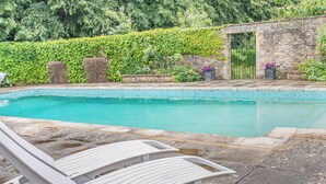 A pool with a white lounge chair in the foreground, surrounded by stone tiles and a stone wall with greenery.