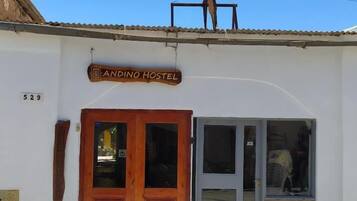 A hostel named "Andino Hostel" with a wooden facade, a stone wall, and a tiled roof.