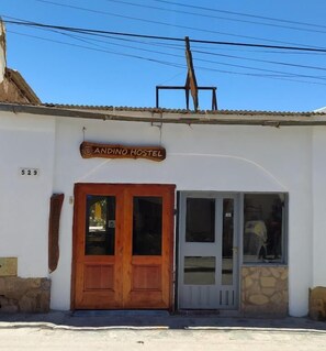 A hostel named "Andino Hostel" with a wooden facade, a stone wall, and a tiled roof.