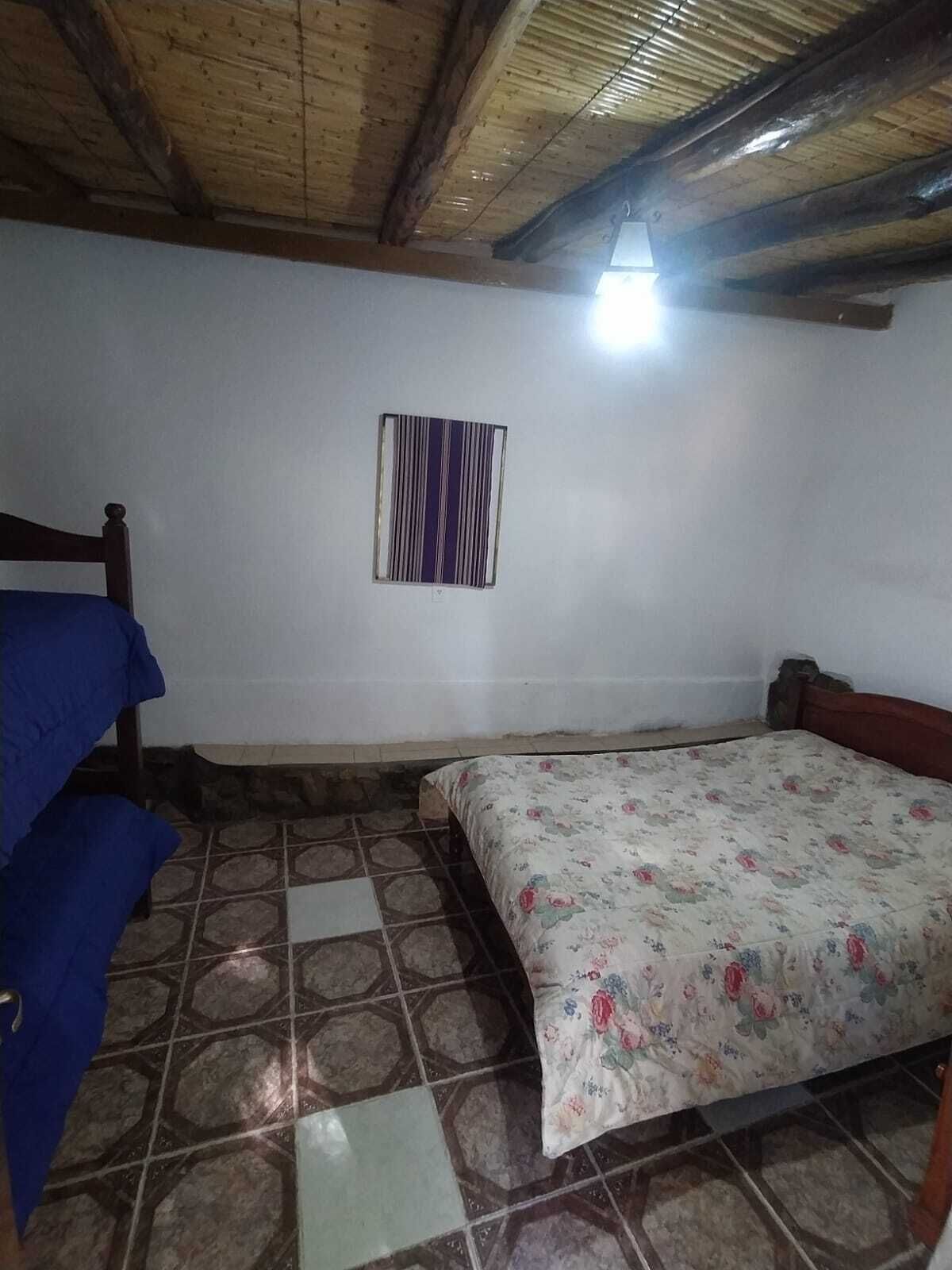 A room with a wooden ceiling, a bed with a floral bedspread, a blue sofa, and a striped wall hanging.