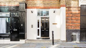 A building facade with a black door, a white wall, and a brick section. - Charming Shoreditch Apartment (London)