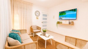 A living room with wicker furniture, a flat-screen TV, and a view of the sea.