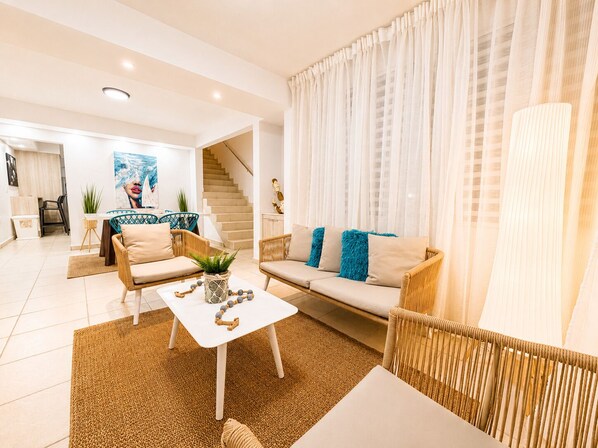 A modern living room with a sofa, chairs, a coffee table, and a staircase leading to another room.