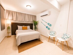 Une chambre à coucher comprenant un lit, une lampe sur pied, une plante en pot, un climatiseur fixé au mur et deux chaises.