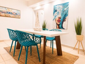 A dining area with a white table, teal chairs, and a painting of a woman.