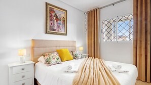 Una habitación de hotel con cama, mesita de noche, ventana con cortinas y un cuadro en la pared.