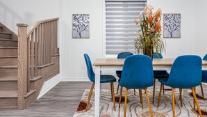 A dining area with a wooden table, blue chairs, a white rug, and a window with blinds. - Luxury Villa 5BR-4.5 Bath (Springwater)