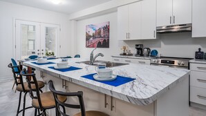 A modern kitchen with white cabinets, a marble countertop, and a central island with bar stools. - Luxury Villa 5BR-4.5 Bath (Springwater)