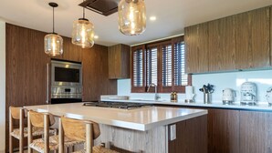 Une cuisine moderne avec des meubles en bois, un grand îlot central, des appareils en acier inoxydable et des luminaires suspendus.