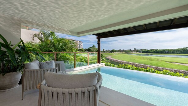 Un espace de détente extérieur moderne, doté d  ’une piscine, de sièges confortables et offrant une vue sur un terrain de golf et un plan d’eau.