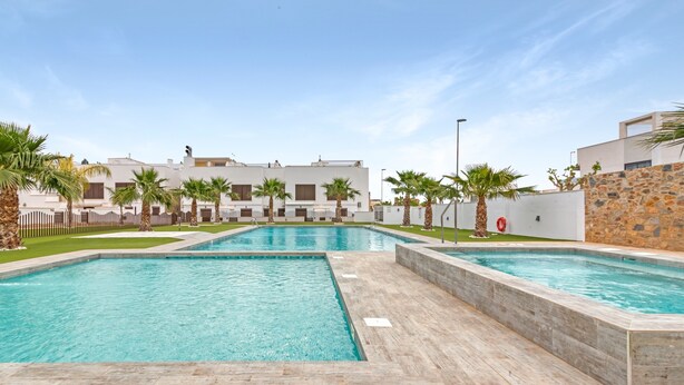 Ein Swimmingpool mit einer Steindeck, umgeben von Palmen und einem weißen Gebäude mit vielen Fenstern.