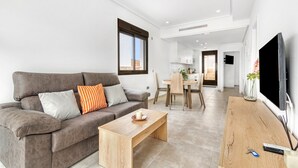Ein modernes Wohnzimmer mit einer Couch, einem Holztisch, einem Fernseher und einem Essbereich mit Tisch und Stühlen.