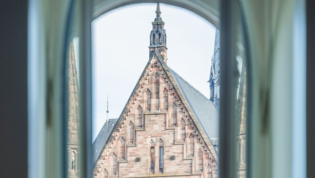 A view through a window of a Gothic-style building with a large rose window and a pointed spire. - Maison Koch · Maison bourgeoise - 240 m2 (Strasbourg)
