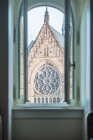 A view through a window of a Gothic-style building with a large rose window and a pointed spire.