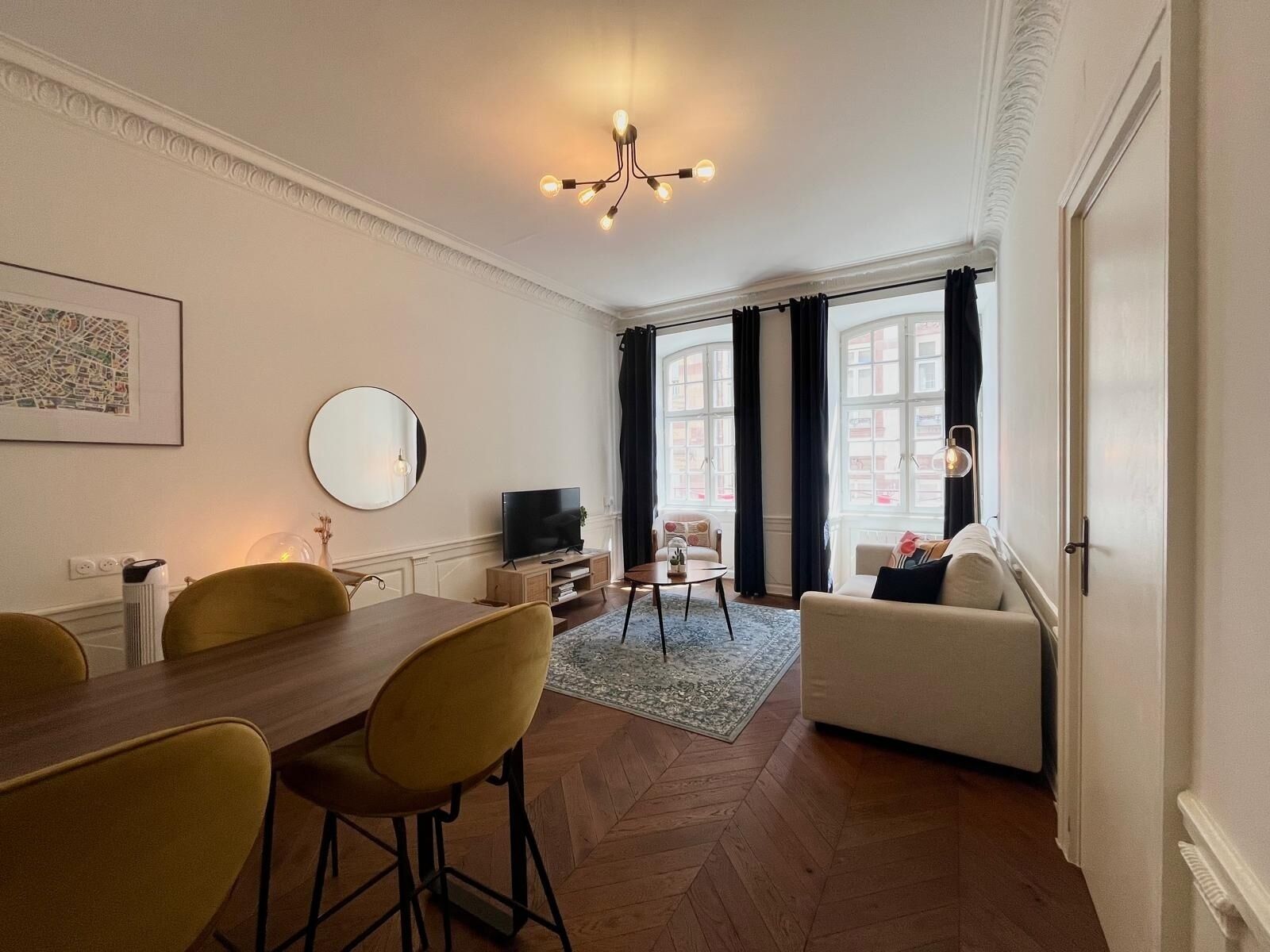 Ein modernes Wohnzimmer mit Essbereich, einem Fernseher und einem großen Fenster mit Vorhängen.