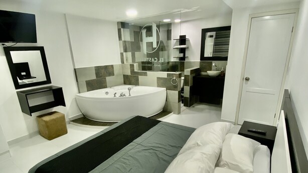 Quarto moderno com cama grande, banheira integrada e banheiro separado com pia e espelho.