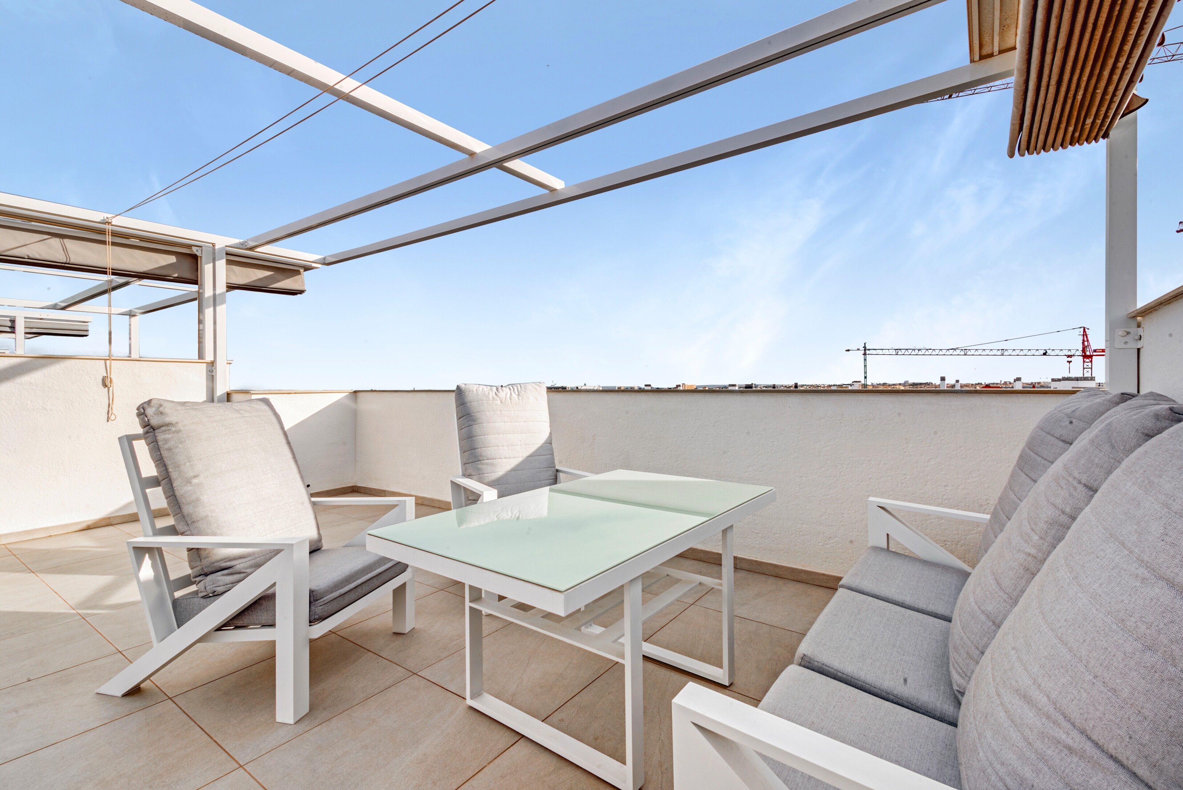 A rooftop terrace with a table and chairs, a pergola, and a view of the construction site in the background.