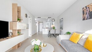 Een moderne woonkamer met een bank, salontafel, televisie en een keuken op de achtergrond.