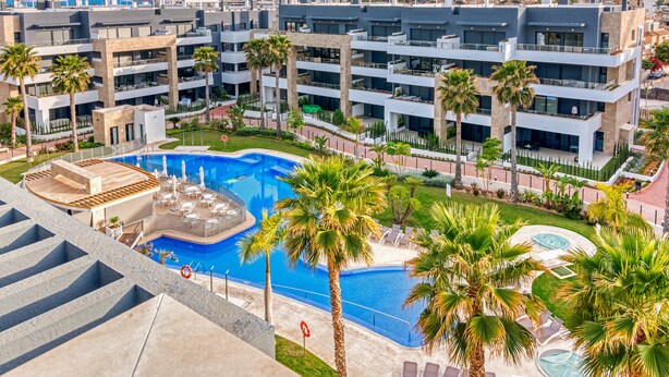 Een modern hotel met een centraal gelegen zwembad, meerdere balkons en palmbomen.