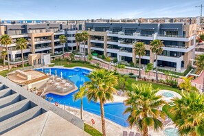 A modern hotel with a central swimming pool, multiple balconies, and palm trees. - Apartment 'Flamenca Village' with Shared Pool, Wi-Fi and Air Conditioning (Orihuela)