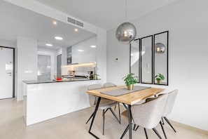 Una cocina moderna con una isla central, una zona de comedor con mesa y sillas de madera, y un espejo grande en la pared.
