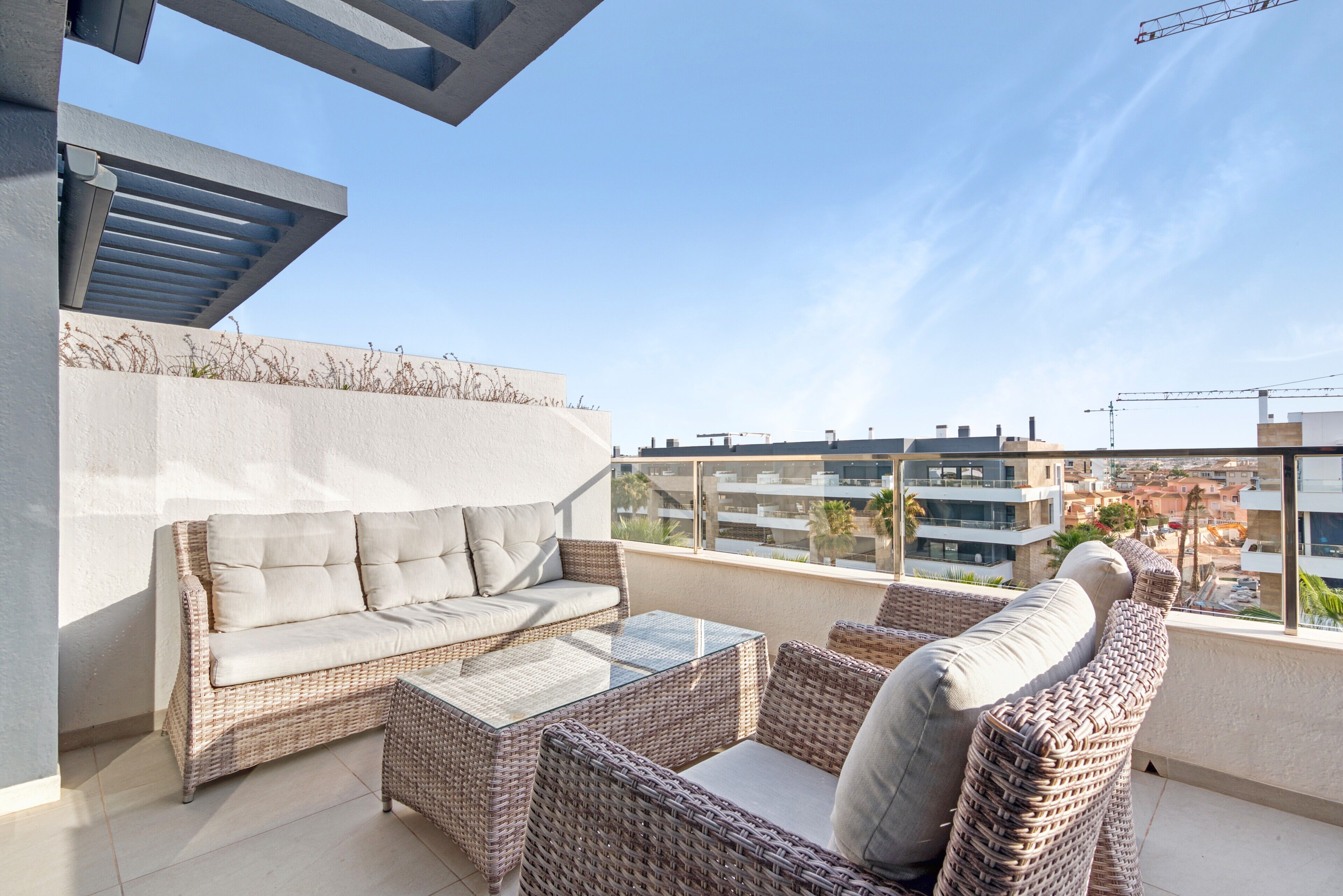 A balcony with a sofa, wicker chairs, and a glass table.