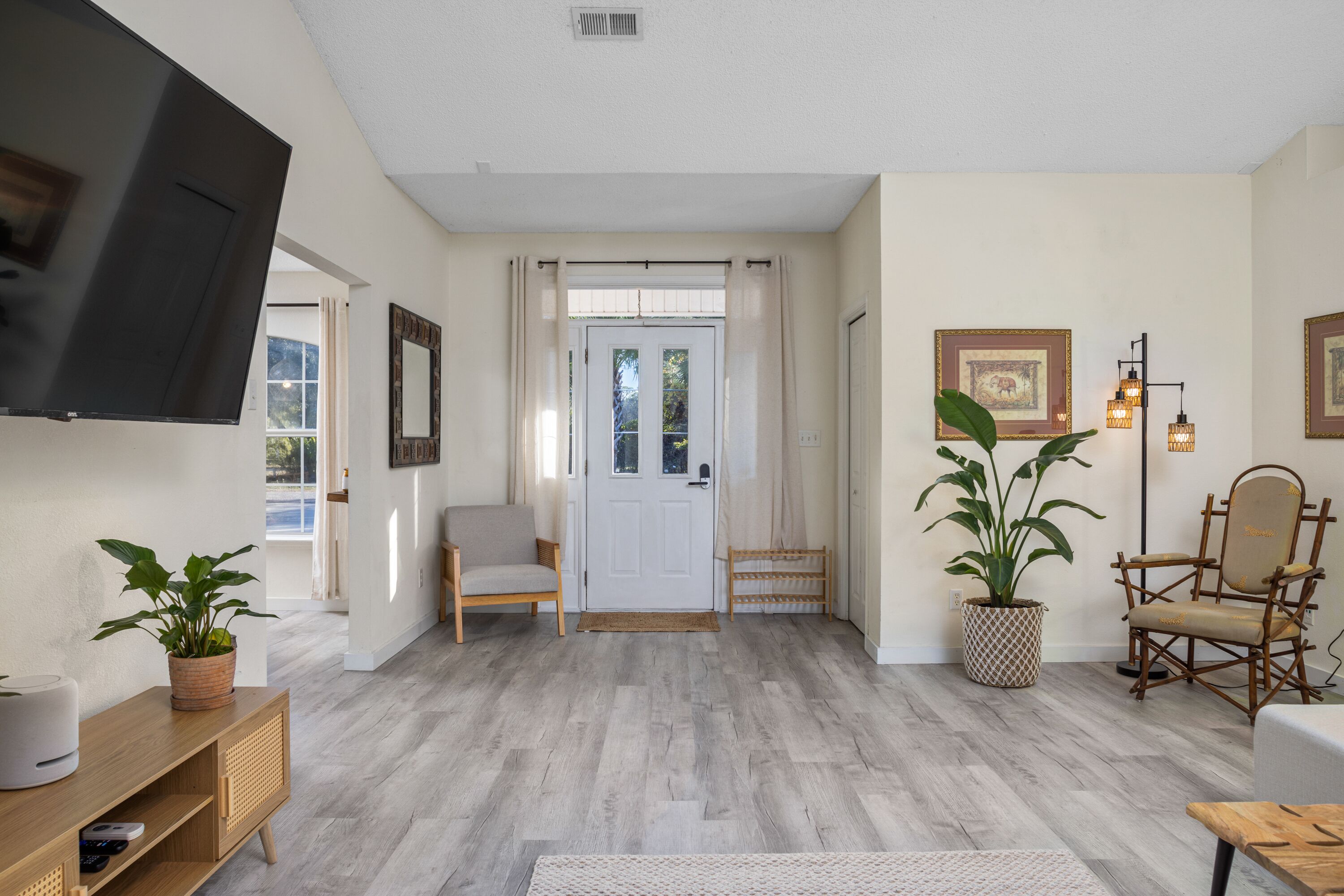 Un salón con televisor, muebles de madera, plantas en macetas y una puerta que da al exterior.