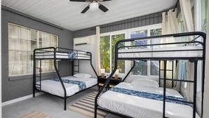 Una habitación con tres literas, un ventilador de techo y ventanas grandes con cortinas.