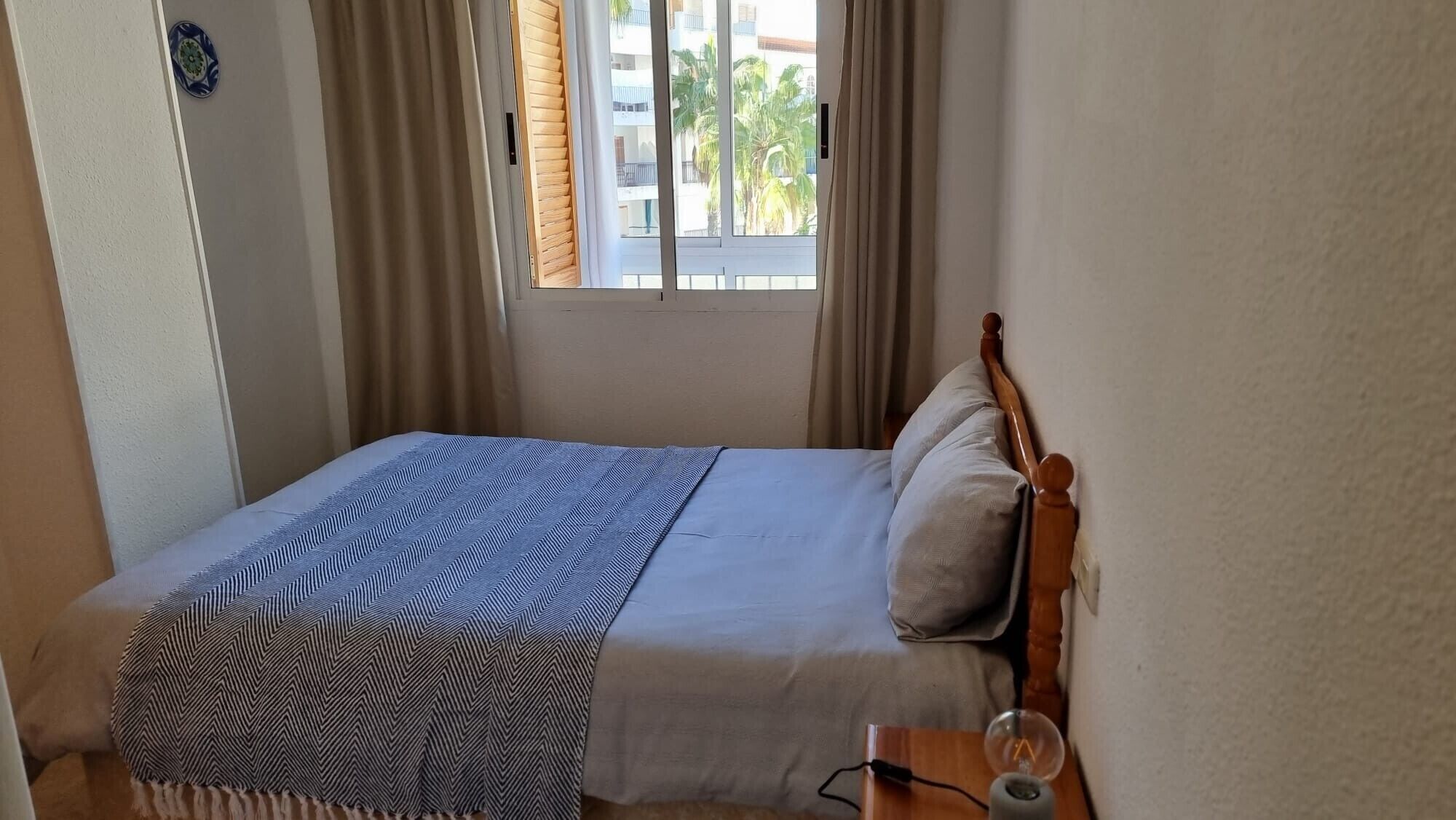 A bed with a striped blanket, a bedside table with a lamp, and a window with curtains.