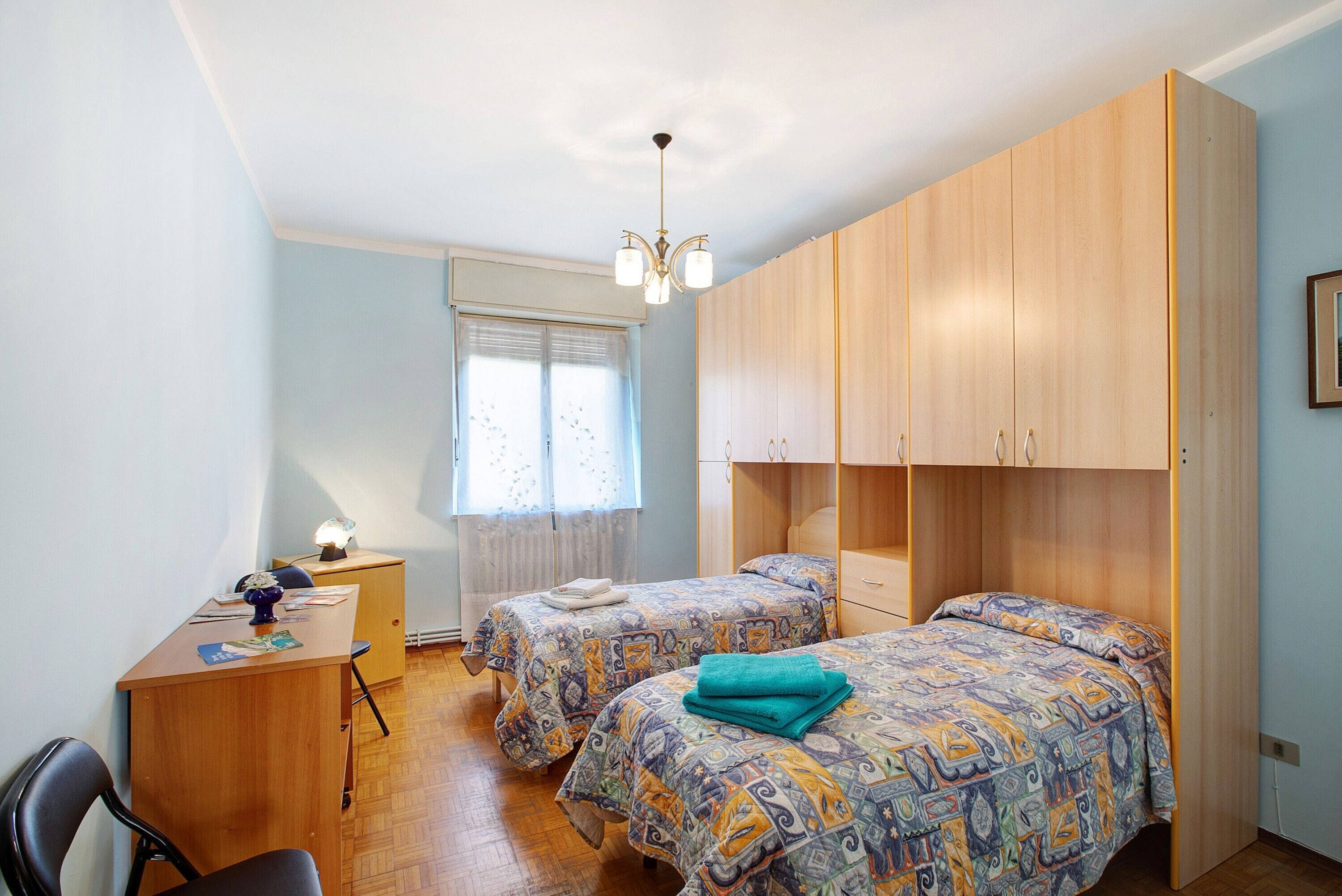 A bedroom with two beds, a desk, a chair, and a wardrobe.