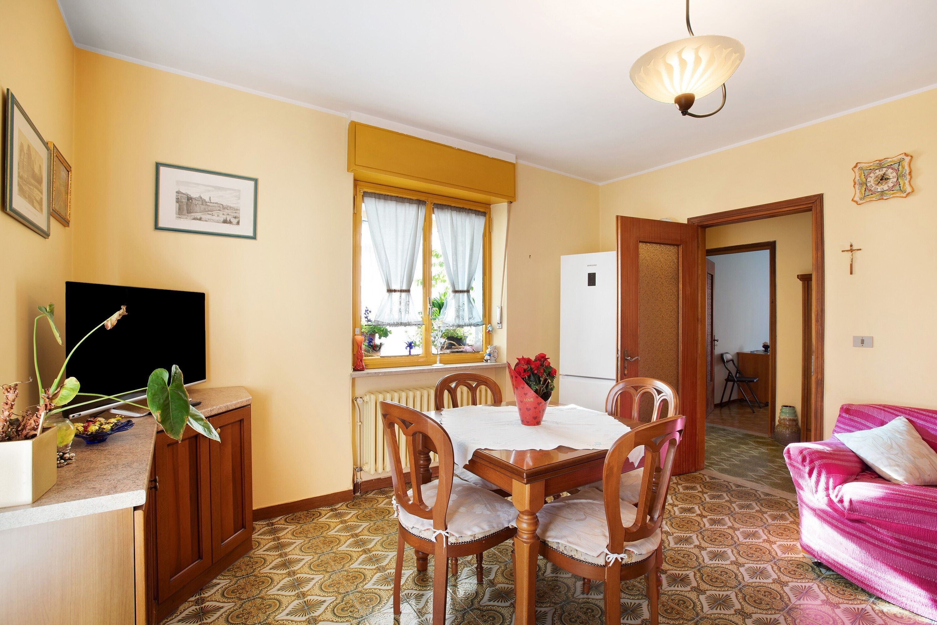 A dining area with a table, chairs, a refrigerator, and a pink sofa.