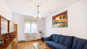 A living room with a blue sofa, wooden flooring, a glass coffee table, a ceiling light fixture, and a painting of a sunset scene. - Apartment 'Maison Blanchet' with Mountain View and Balcony (Sarre)