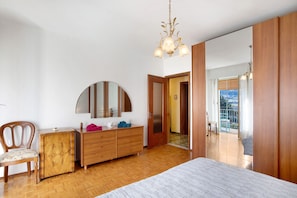 Una camera da letto con una cassettiera in legno, una sedia, un letto, uno specchio e un lampadario.