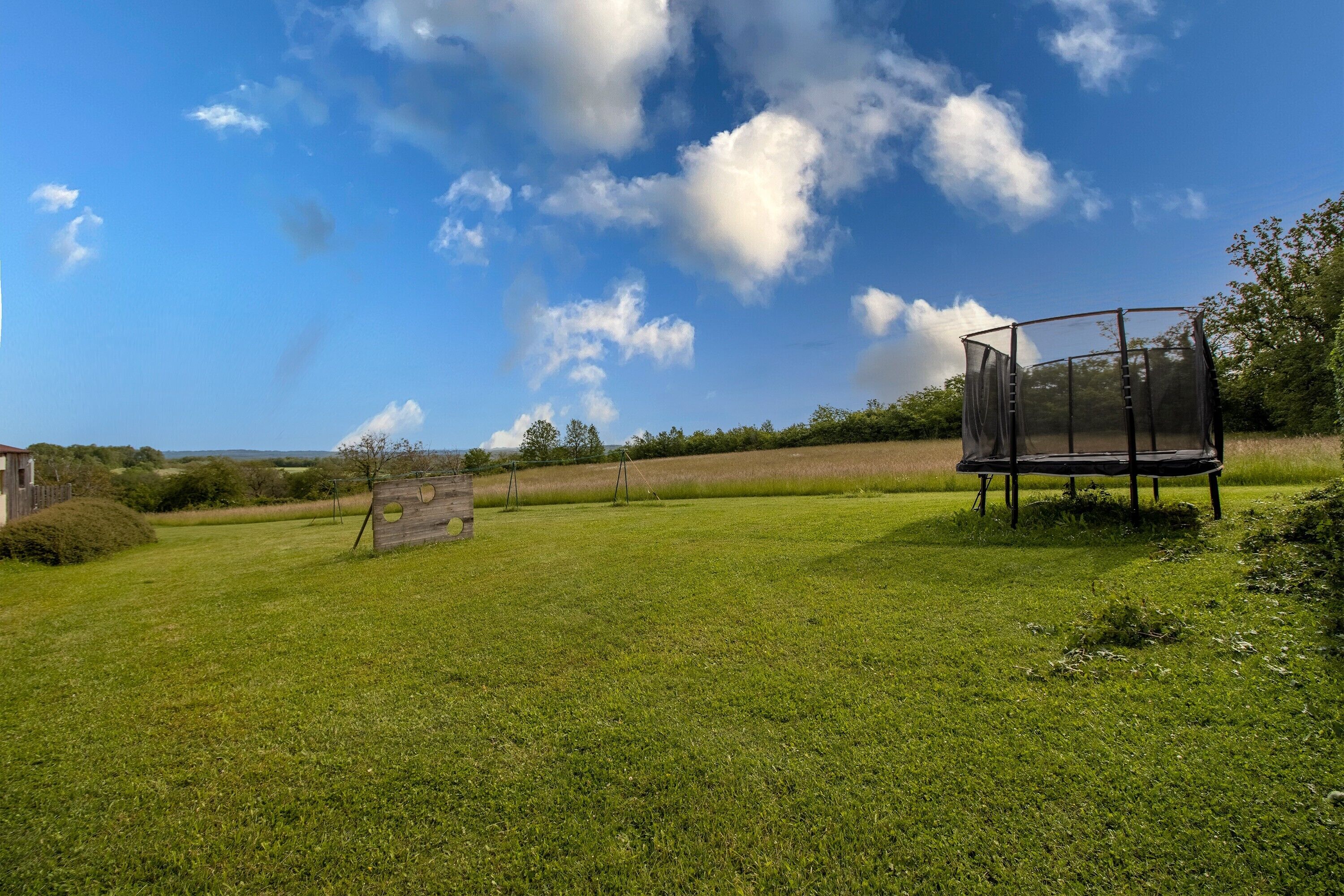 A grassy field with a trampoline and a wooden structure.